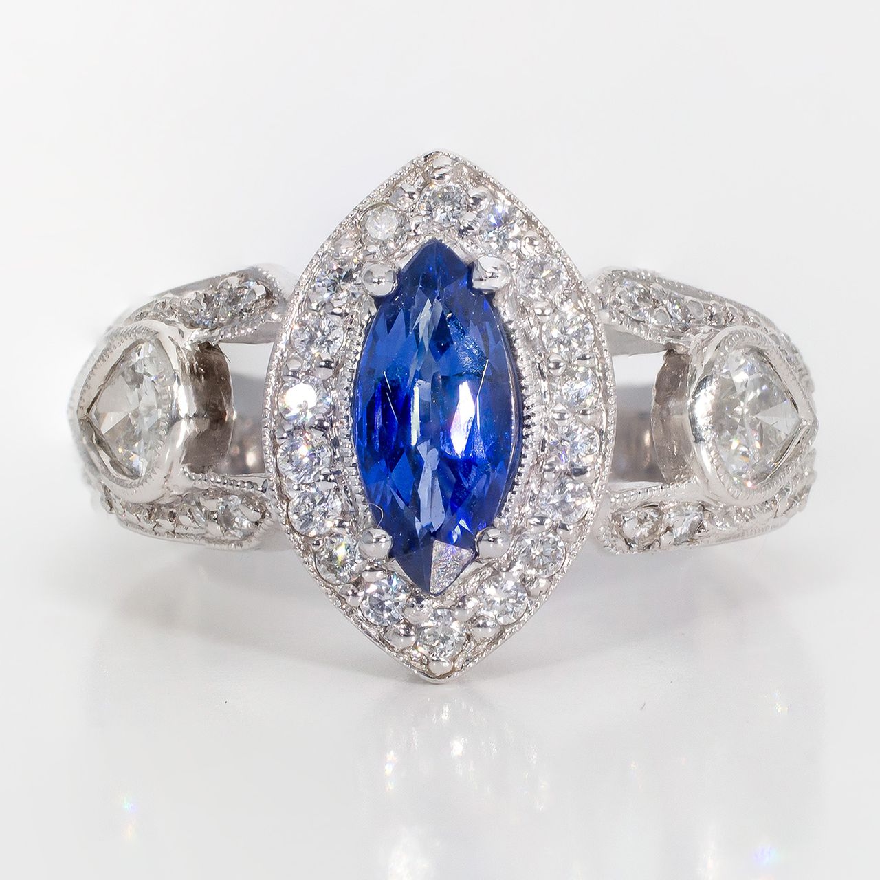 Halo ring in platinum with with bezel set pear shape sides, pave set round diamonds around 4-prong set marquise shaped sapphire center stone.  D1.20ct.t.w.  Sapphire 1.04ct.